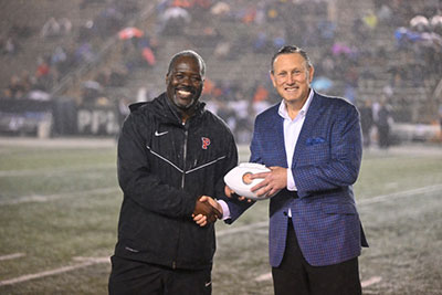 Dr. Marc Levine and John Mack on the Princeton football field, Dr. Levine is holding a football and shaking the hand of John Mack